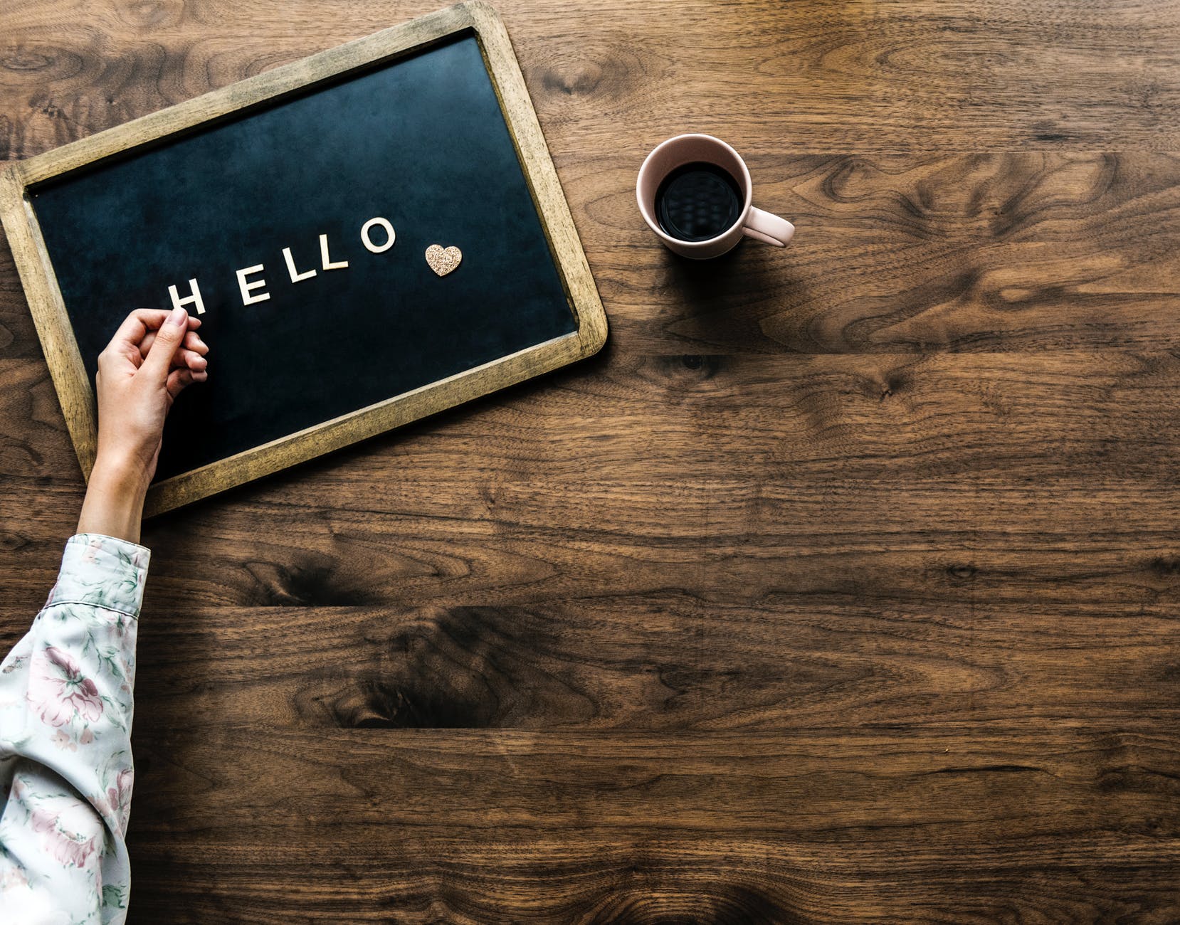 person s hand on black board with hello text beside brown mug